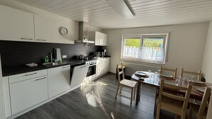 A modern kitchen with white cabinets, a black countertop, and a dining area with a table and chairs. - Vidi Apartmens: By the stream (Bad Überkingen)