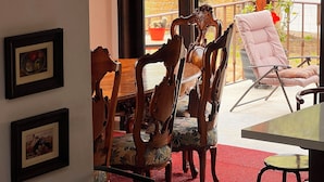 A dining area with wooden chairs and a table, a red rug, and a view of a garden through large windows. - La marquesa casa hotel (Villa de Leyva)