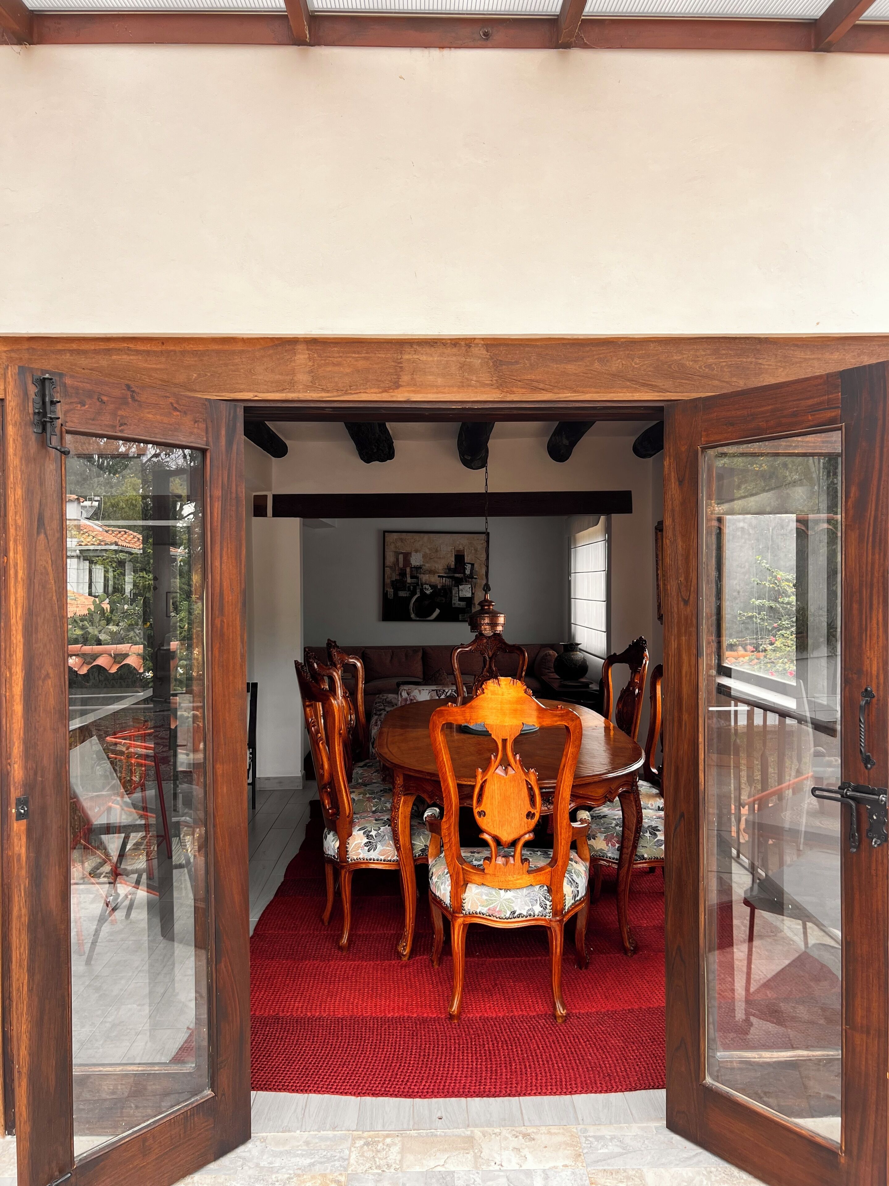 Un coin repas avec une table et des chaises en bois, une moquette rouge et une vue à travers des portes vitrées.
