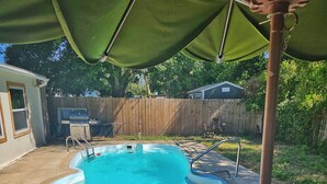Un jardin avec une piscine, un patio couvert et une clôture en bois.