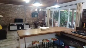 A kitchen with a large island, bar stools, a TV, and a dining area with chairs. - Beach House in Cassino RS (Rio Grande)