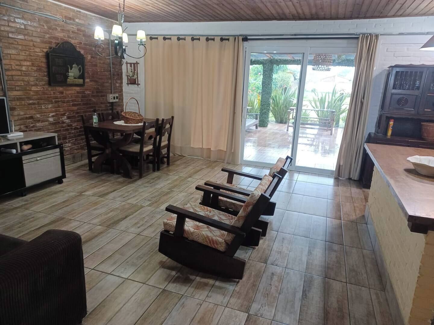 A cozy living area with a wooden bench, a dining table with chairs, a kitchen counter, and a sliding glass door leading to an outdoor patio.