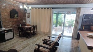 A cozy living area with a wooden bench, a dining table with chairs, a kitchen counter, and a sliding glass door leading to an outdoor patio. - Beach House in Cassino RS (Rio Grande)