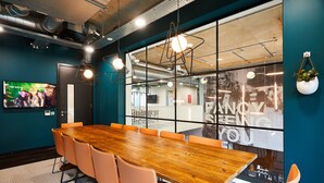A conference room with a wooden table and orange chairs, large windows with a view, and modern lighting fixtures. - Student Only Vita St. Albans (Leeds)