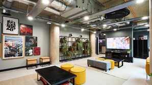 A modern lounge area with a black table, yellow ottomans, a large TV, and artwork on the walls. - Student Only Vita St. Albans (Leeds)
