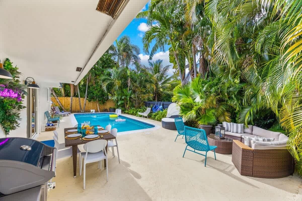 A poolside area with a dining table, chairs, a barbecue grill, and lounge seating.