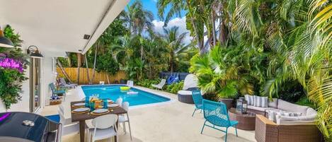 A poolside area with a dining table, chairs, a barbecue grill, and lounge seating.