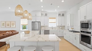 A modern kitchen with white cabinetry, a central island, and a brown leather sofa. - Family-friendly Coastal Escape Grill, Decks & More! (Santa Rosa Beach)
