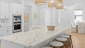 Une cuisine moderne avec des meubles blancs, un îlot central et un coin repas doté de chaises en osier.