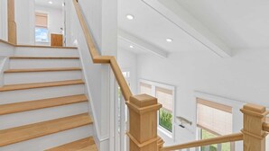Un escalier avec des marches en bois et une rampe en bois, menant à un étage supérieur d’où l’on peut admirer la verdure environnante.