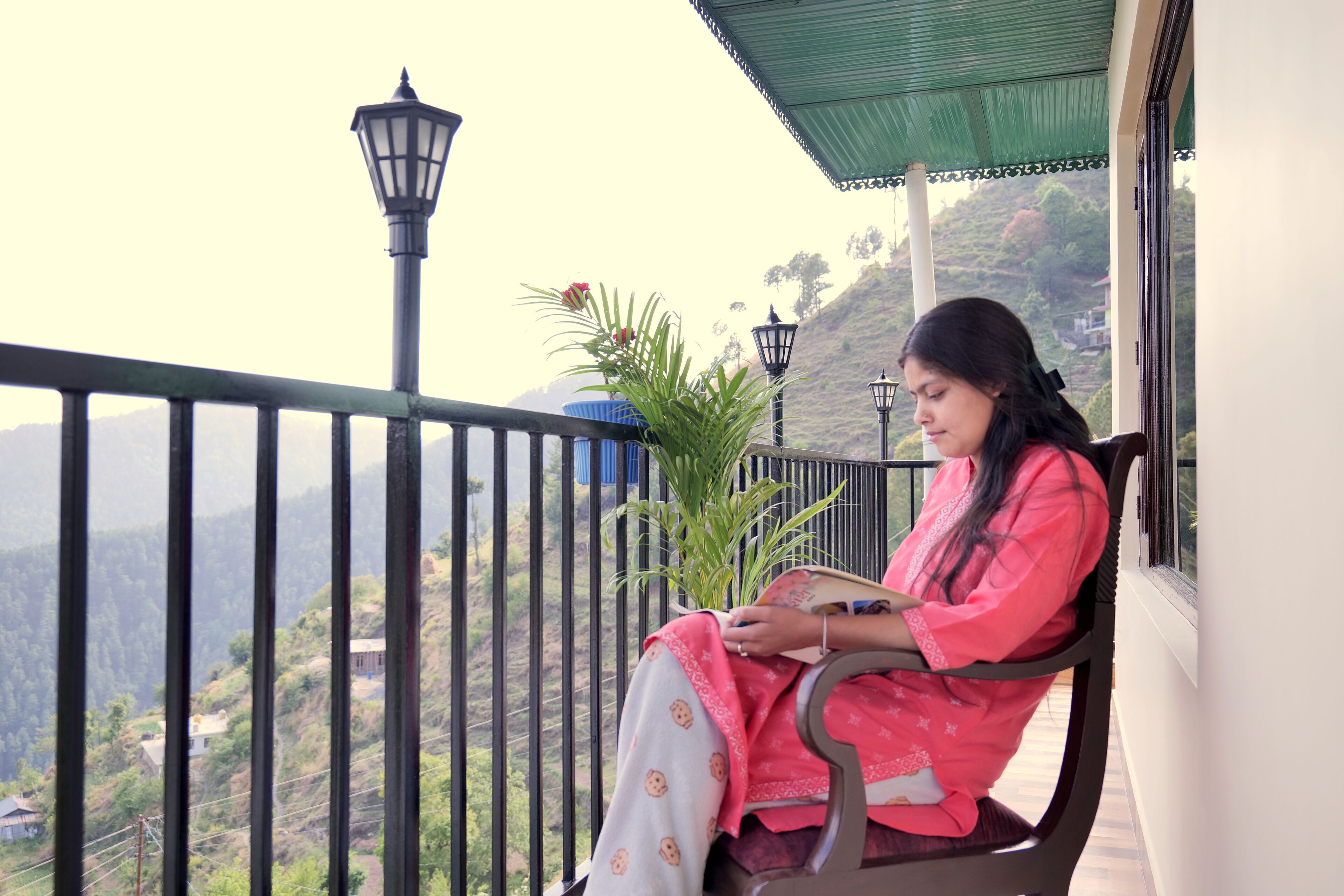 A woman sitting on a balcony with a view of a mountainous landscape.