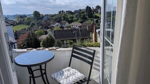 Un balcon avec une table ronde et une chaise, donnant sur un quartier résidentiel avec des maisons et de la verdure.