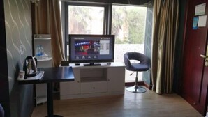 A room with a TV, a chair, a small table with a kettle, and a window with curtains. - Dishuiwan Fashion Hotel (Shanghai)