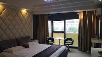 A hotel room with a large bed, two chairs, a small table, and a view of the outside.