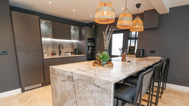 A modern kitchen with a marble island, black chairs, and wicker pendant lights. - Ty Blodau (Prestatyn)