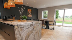 A modern kitchen with a marble island, black cabinets, and a dining area with a large window overlooking a garden. - Ty Blodau (Prestatyn)