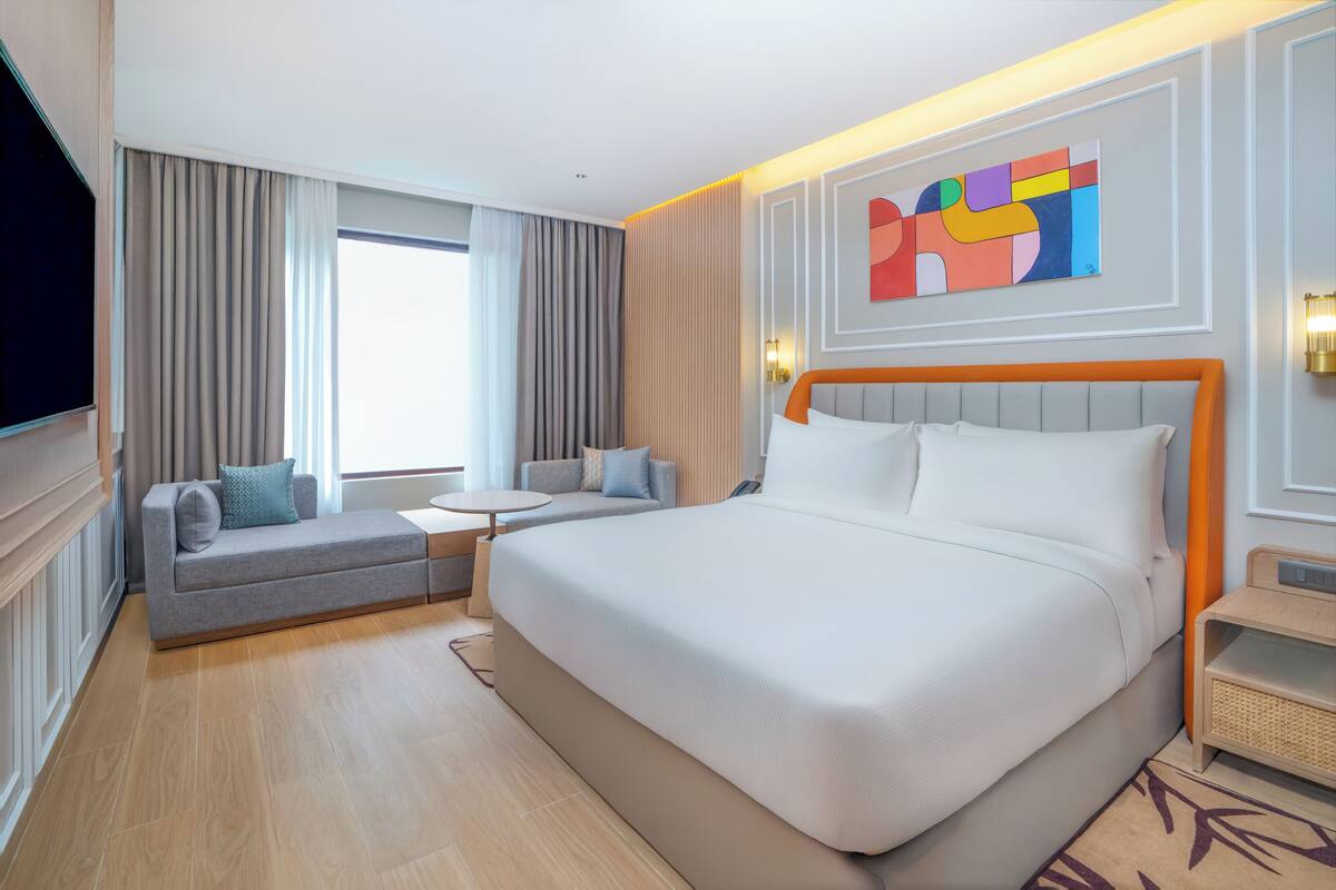A hotel room with a large bed, a sofa, a small table, and a TV.