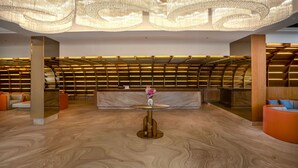 Een moderne lobby met een marmeren vloer, een ronde tafel met een vaas en een zithoek met oranje stoelen.