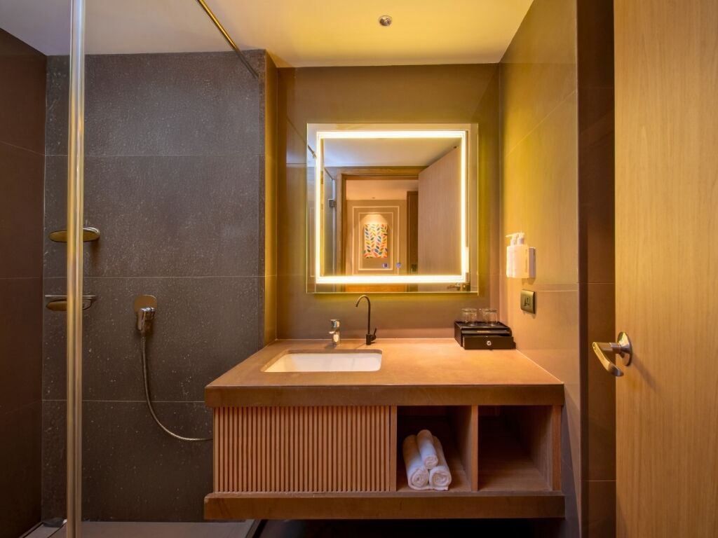 A modern bathroom with a wooden vanity, a glass shower enclosure, and a mirror with a lighted frame.