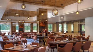 Een ruim restaurant met meerdere eettafels en stoelen, een houten plafond en grote ramen.