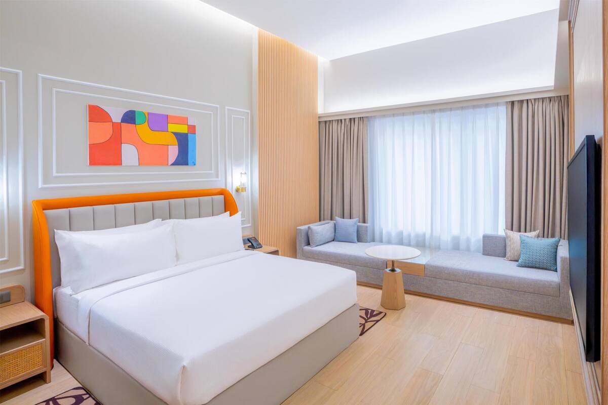 A hotel room with a bed, a sofa, a TV, and a painting on the wall.
