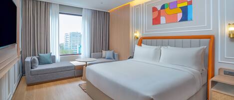 Habitación de hotel con una cama grande, un sofá, una mesita y un televisor.