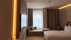 Een hotelkamer met een groot bed, een bank, een televisie en een raam met gordijnen.