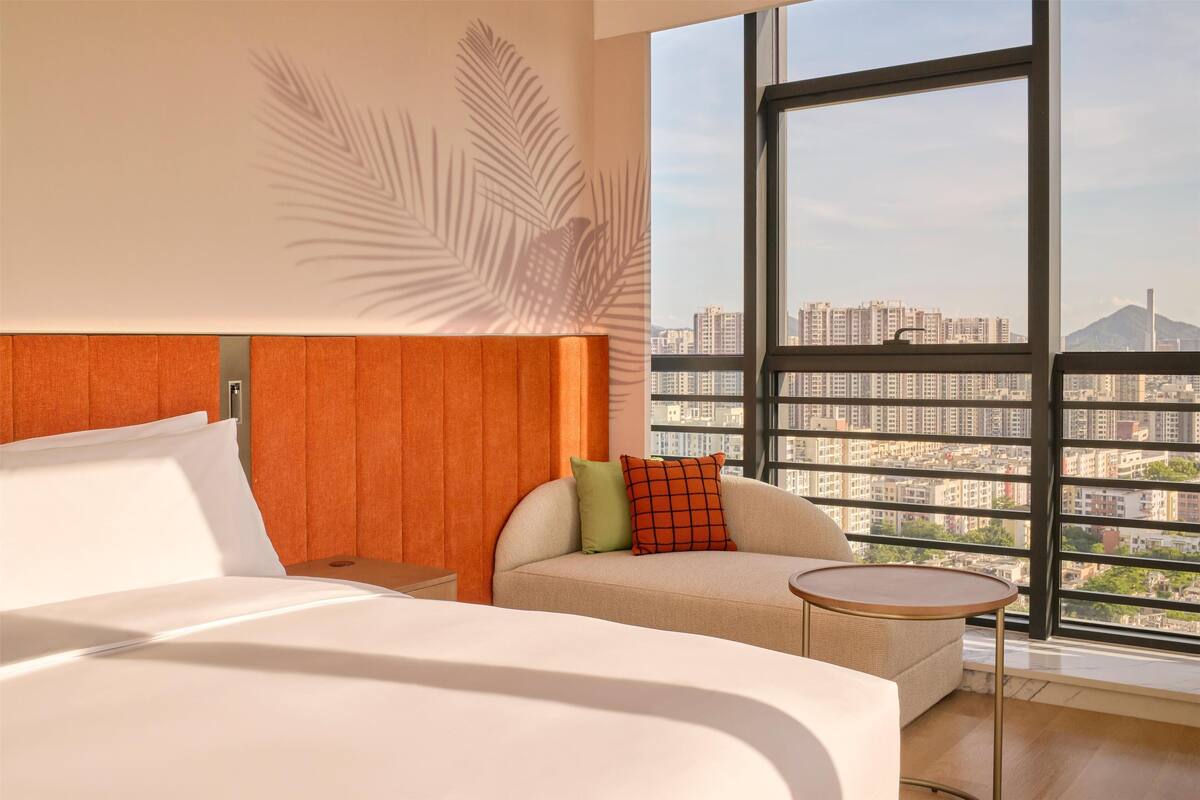 Een hotelkamer met een groot raam, een bed, een bank en een kleine tafel.