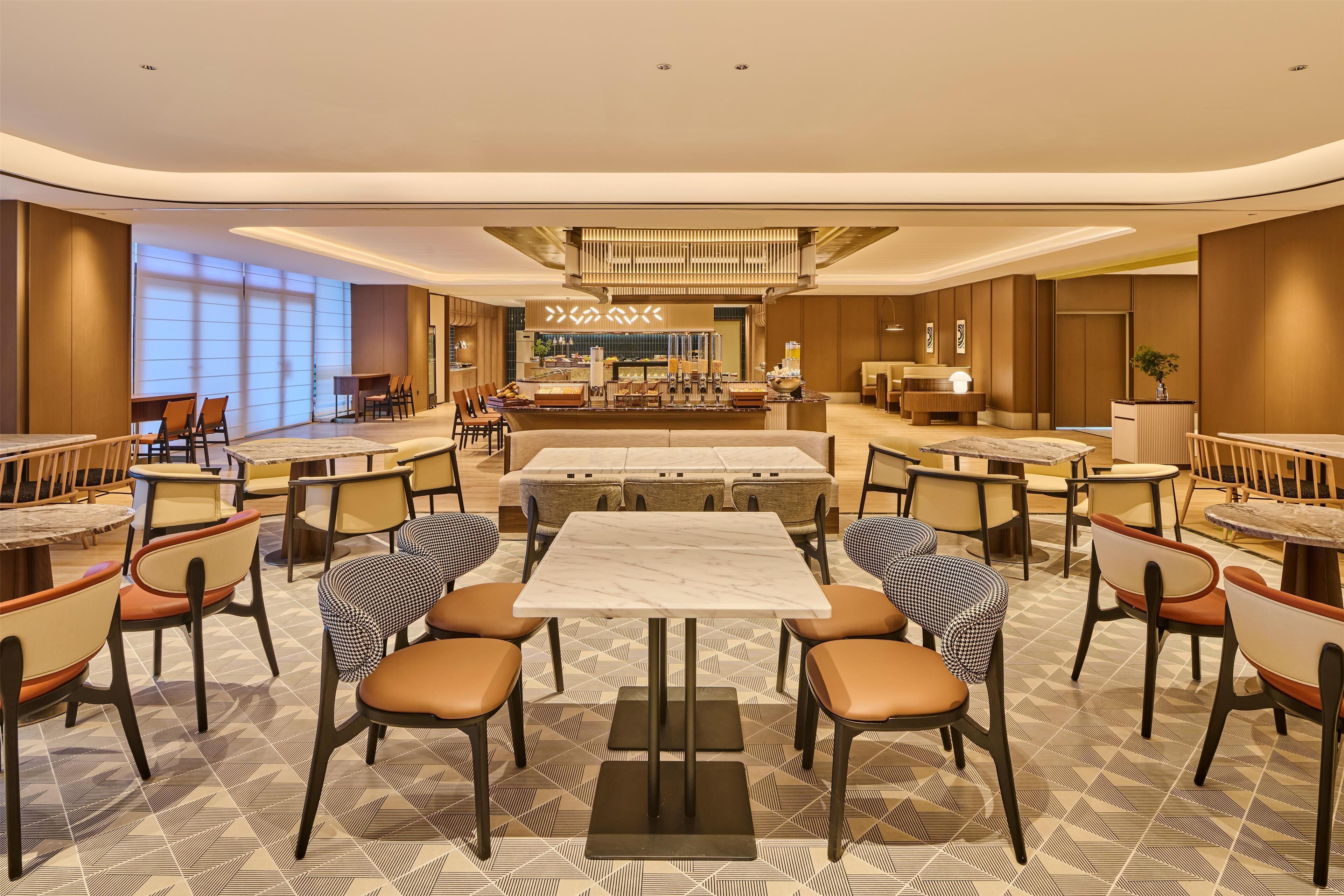 Un espace de restauration moderne doté d’un bar central, de plusieurs types d’aménagements pour s’asseoir et d’un sol à motifs.