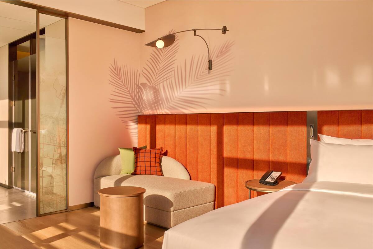 Een hotelkamer met een bed, een zithoek met een stoel en een tafeltje, een glazen scheidingswand en een aan de muur bevestigd telefoon.