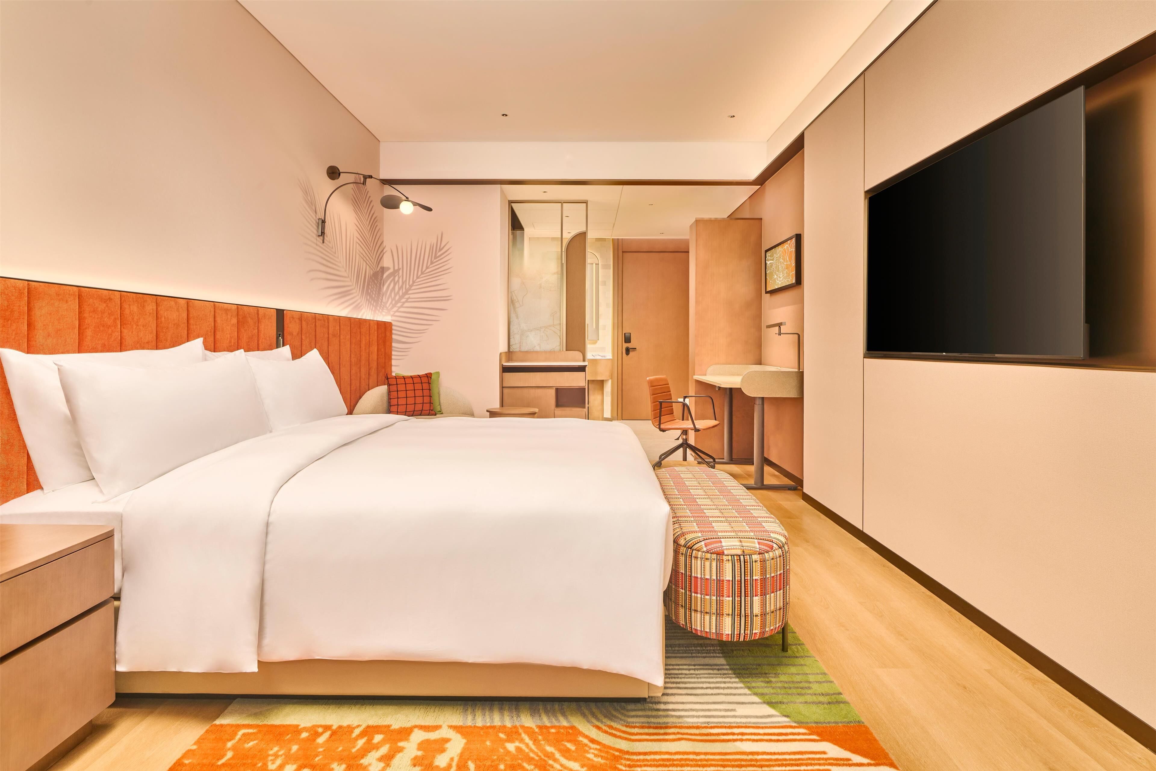 Habitación de hotel moderna con una cama grande, televisión, escritorio y baño a la vista a través de una puerta abierta.
