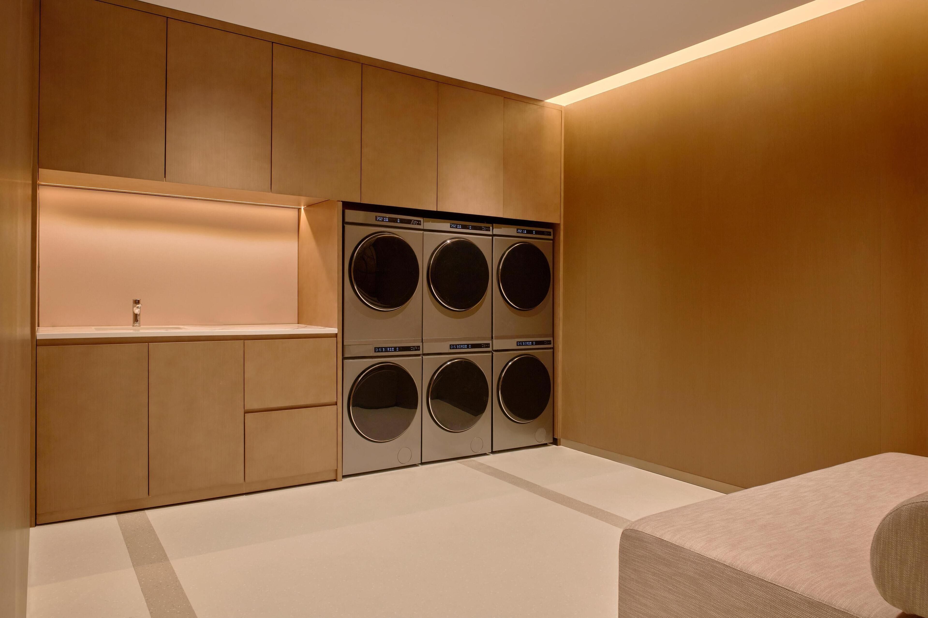 A laundry room with six washing machines, a sink, and a bench.