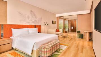 A modern hotel room with a large bed, a bench, a desk, and a chair.