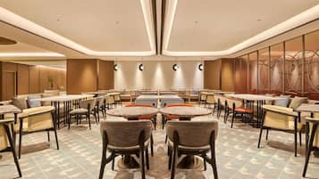A spacious dining area with round tables and chairs, a patterned floor, and modern ceiling lighting.