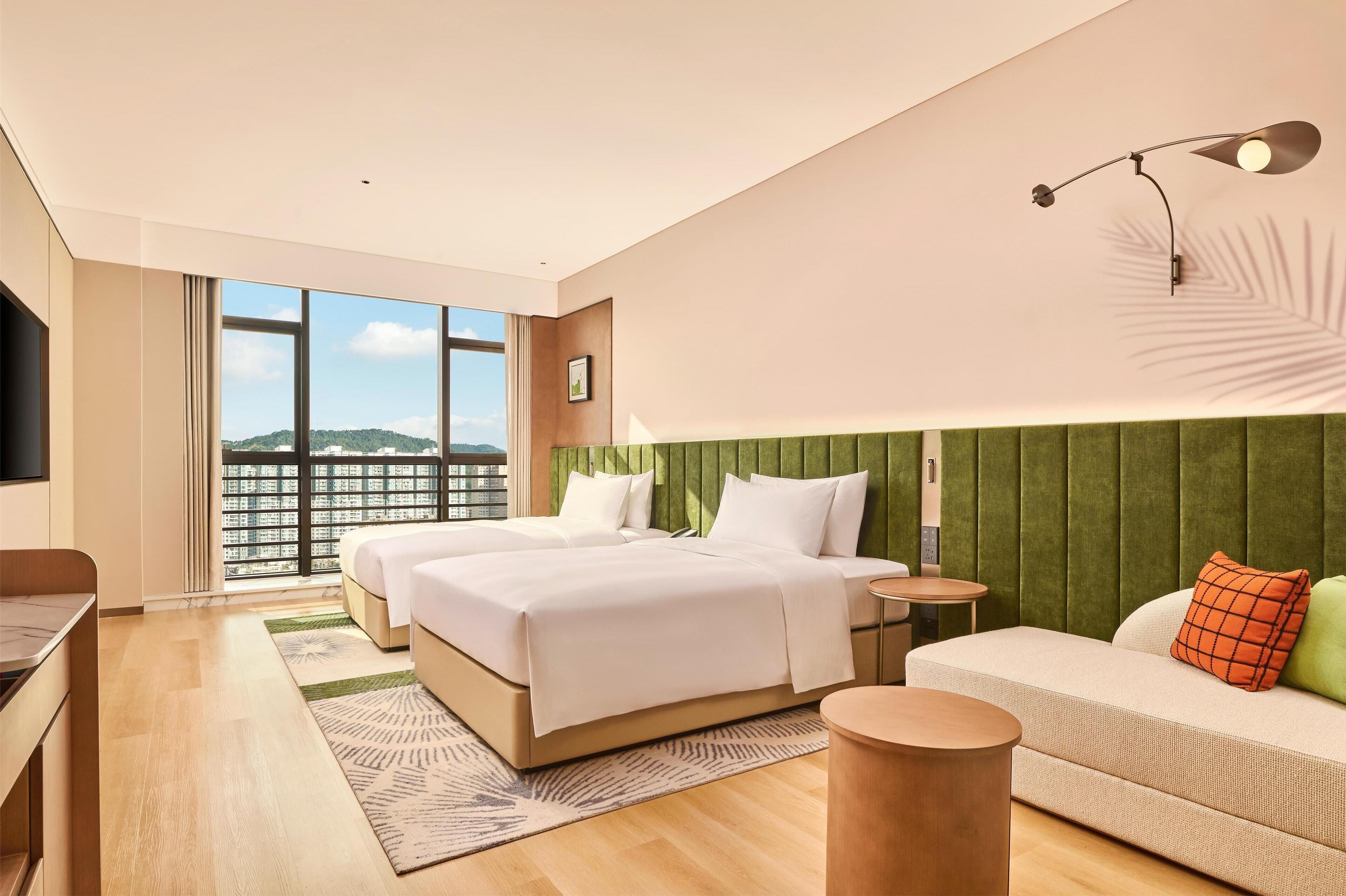 Habitación de hotel moderna con una cama grande, un sofá, un escritorio y vistas a la ciudad.