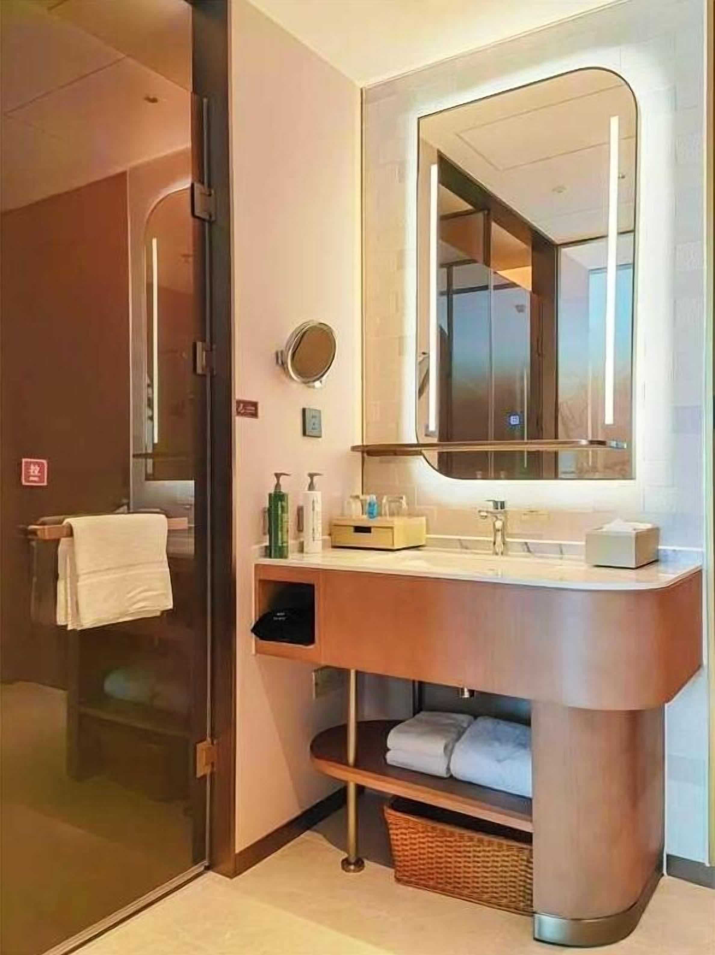 Un baño moderno con cabina de ducha de vidrio, tocador de madera con espejo y perchero.