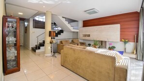 Ein modernes Wohnzimmer mit einem beigefarbenen Sofa, einem Glastisch und einer Treppe, die in ein Obergeschoss führt. Auf dem Seitentisch befinden sich Blumentöpfe und eine dekorative Vase.