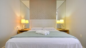 Ein ordentlich bezogenes Bett mit weißen Leinen, zwei Nachttischlampen und ein Spiegel darüber.