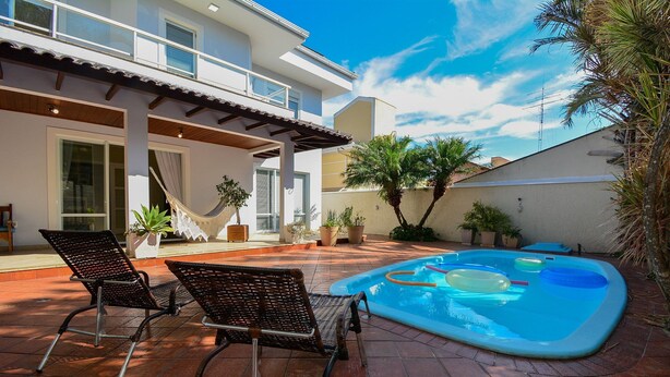 Ein modernes Haus mit Schwimmbecken, zwei Liegestühlen und einer Hängematte.