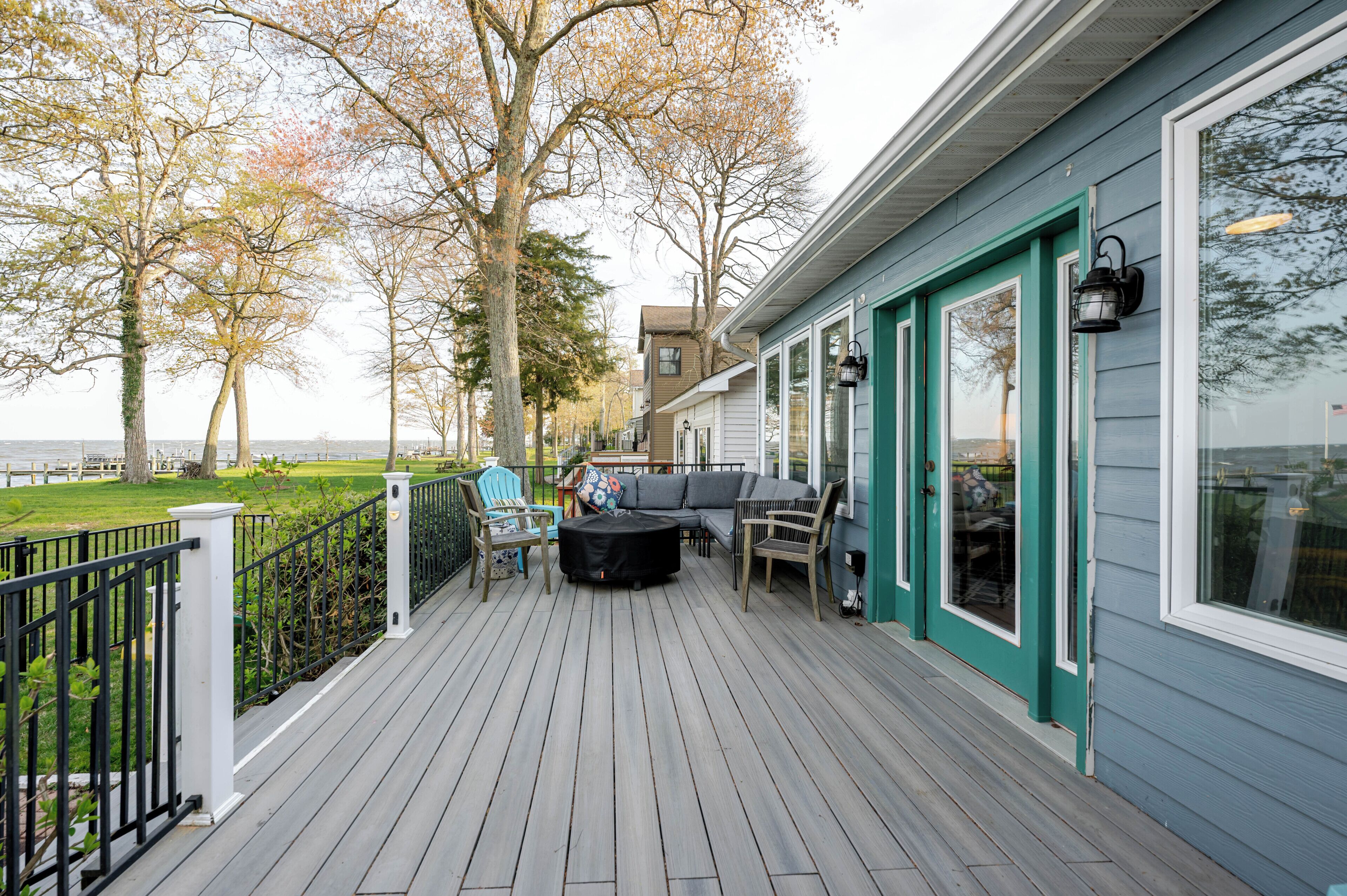A deck with outdoor seating, a view of the water, and a building with teal trim and large windows.