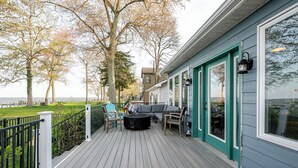 A deck with outdoor seating, a view of the water, and a building with teal trim and large windows.