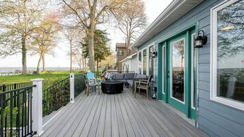 A deck with outdoor seating, a view of the water, and a building with teal trim and large windows.
