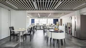 A modern dining area with multiple tables and chairs, a kitchen area with a refrigerator, and a view through the window.