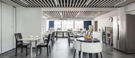 A modern dining area with multiple tables and chairs, a kitchen area with a refrigerator, and a view through the window.