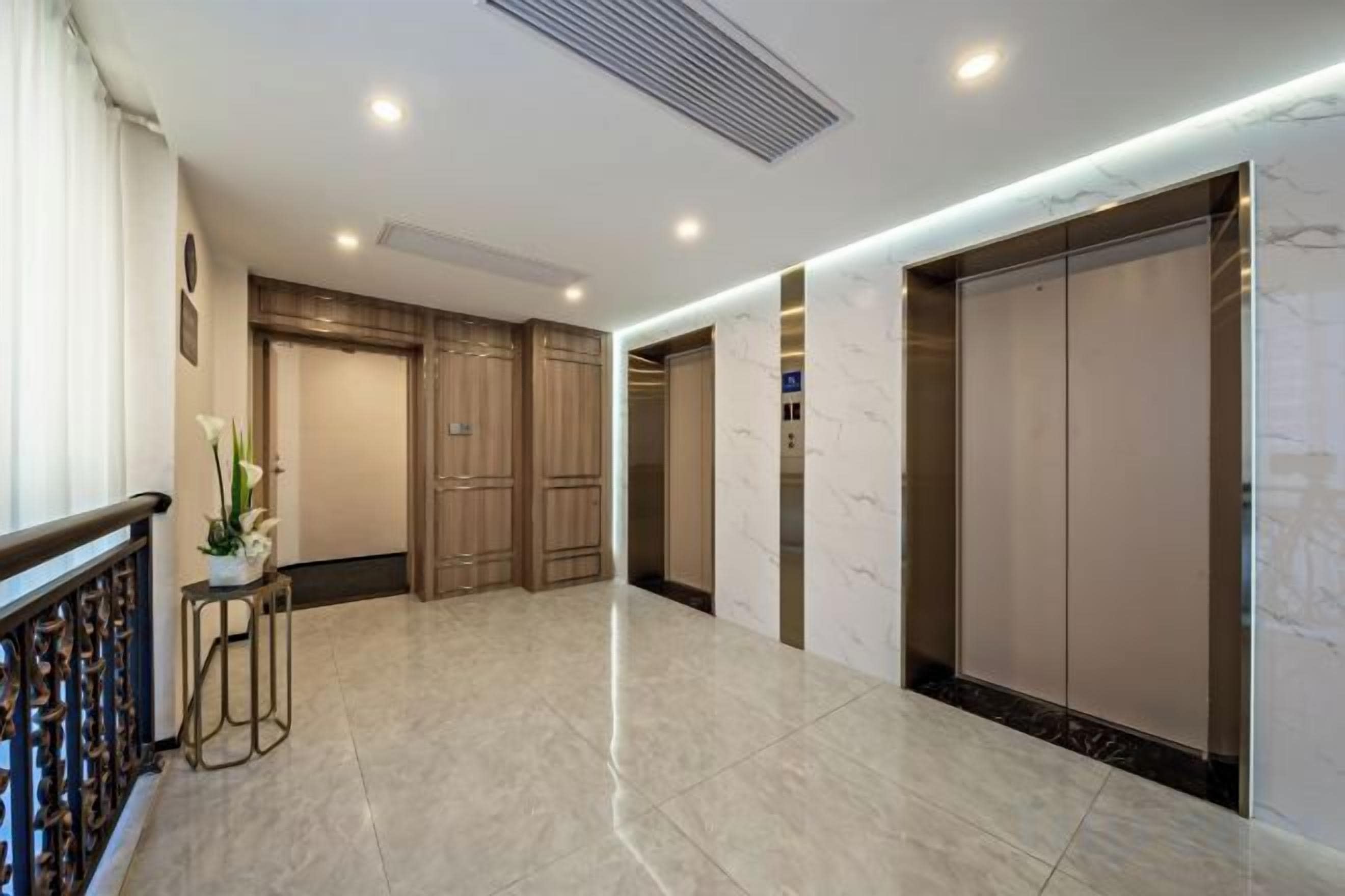 Un vestíbulo de hotel con piso de mármol, puertas de madera y un moderno ascensor.