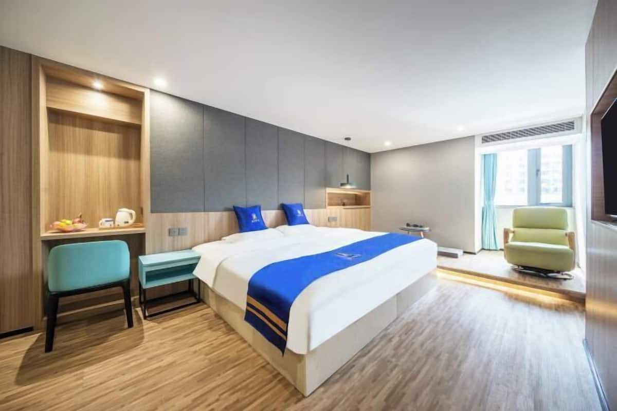 A hotel room with a bed, a desk, a chair, a TV, and a window.