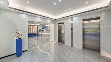 Un hall d’entrée moderne avec un sol en marbre, un comptoir de réception et deux ascenseurs.