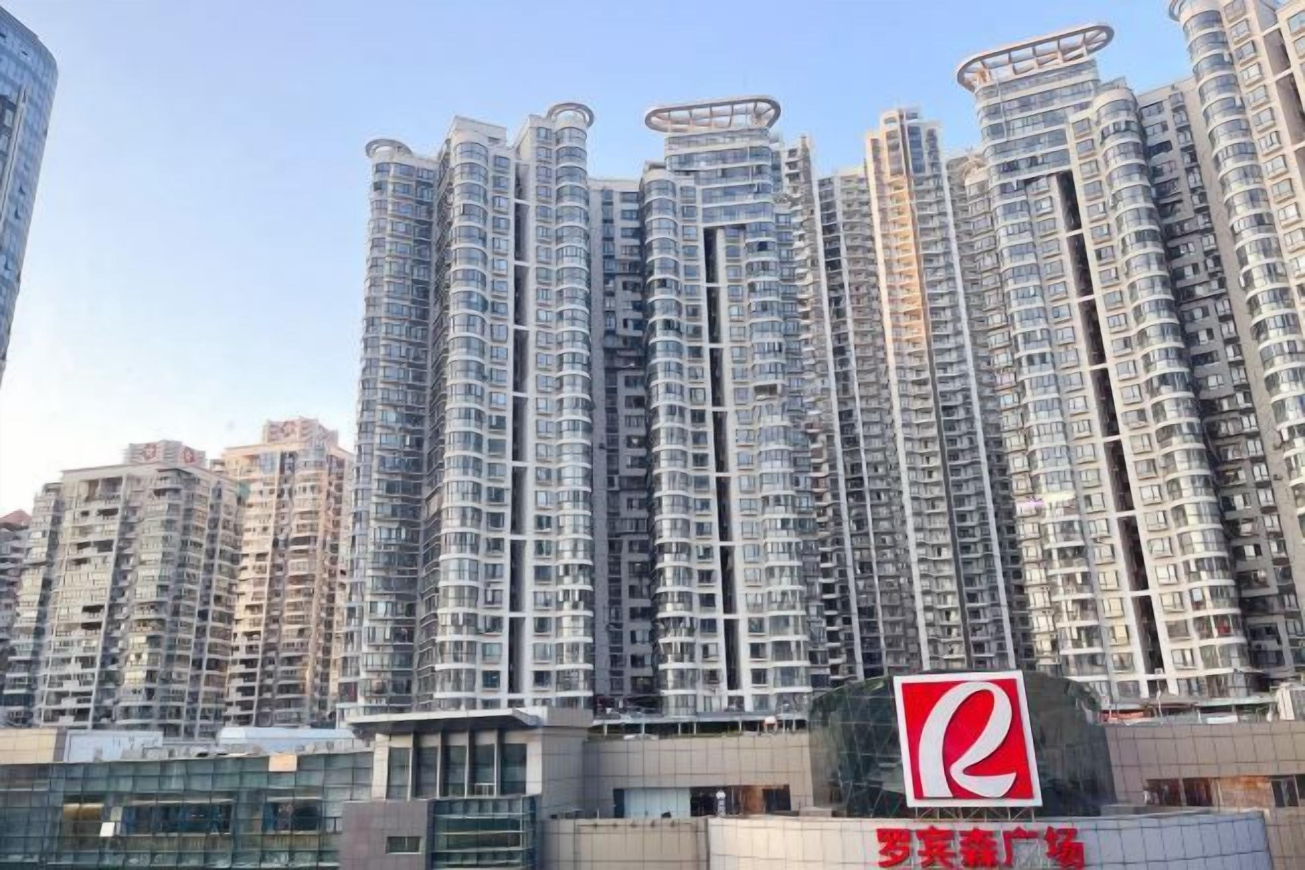 Een hoog appartementencomplex met meerdere balkons, een opvallend logo en een hekpoort.