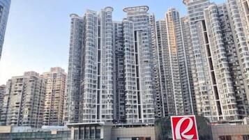 A high-rise residential building with multiple balconies, a prominent logo, and a gated entrance.