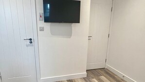 Una habitación con una televisión de pantalla plana en la pared, un sofá azul y un piso de madera en patrón de espiga.